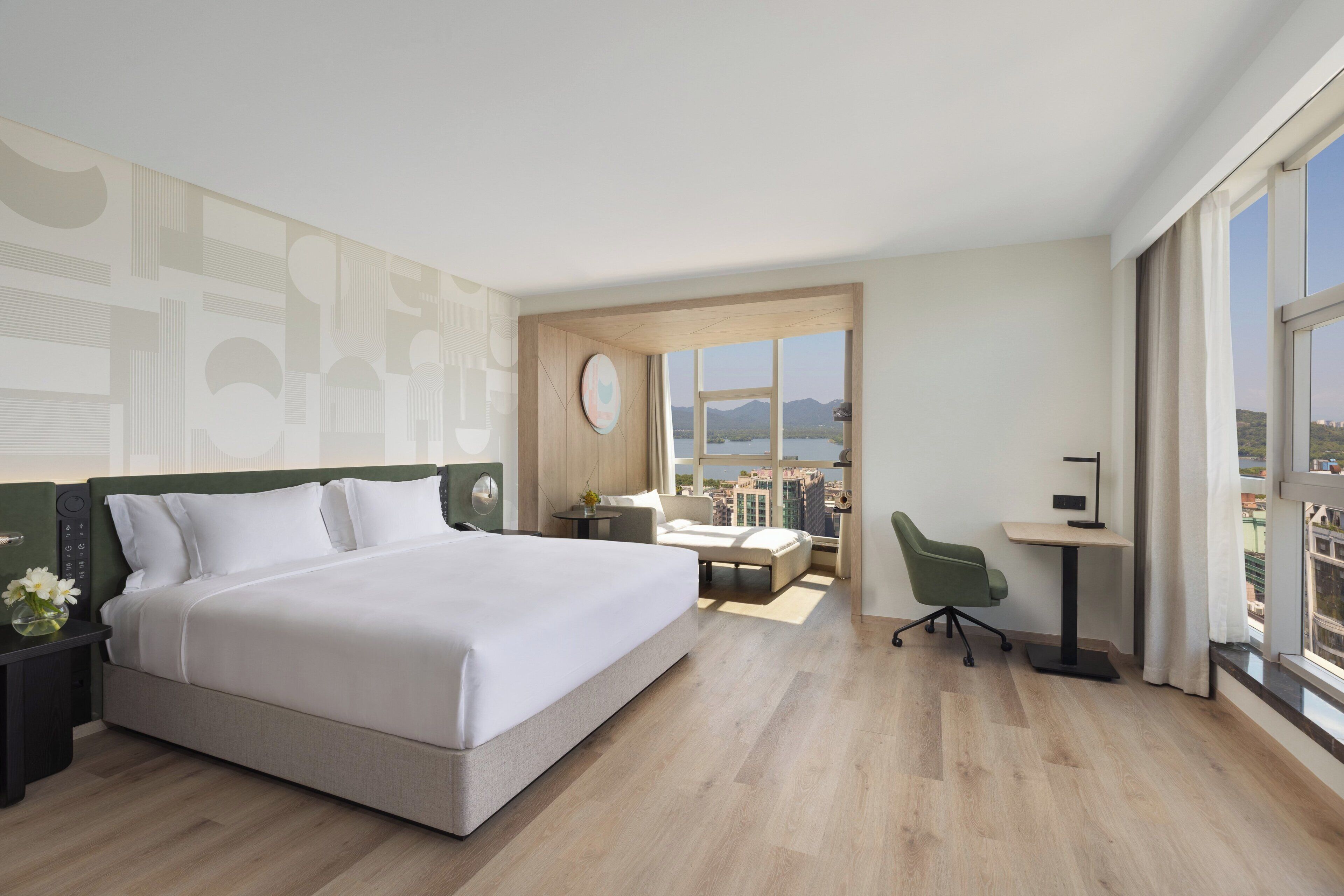 Habitació d'hotel moderna amb un llit gran, una taula de treball, una cadira i vista a la ciutat.