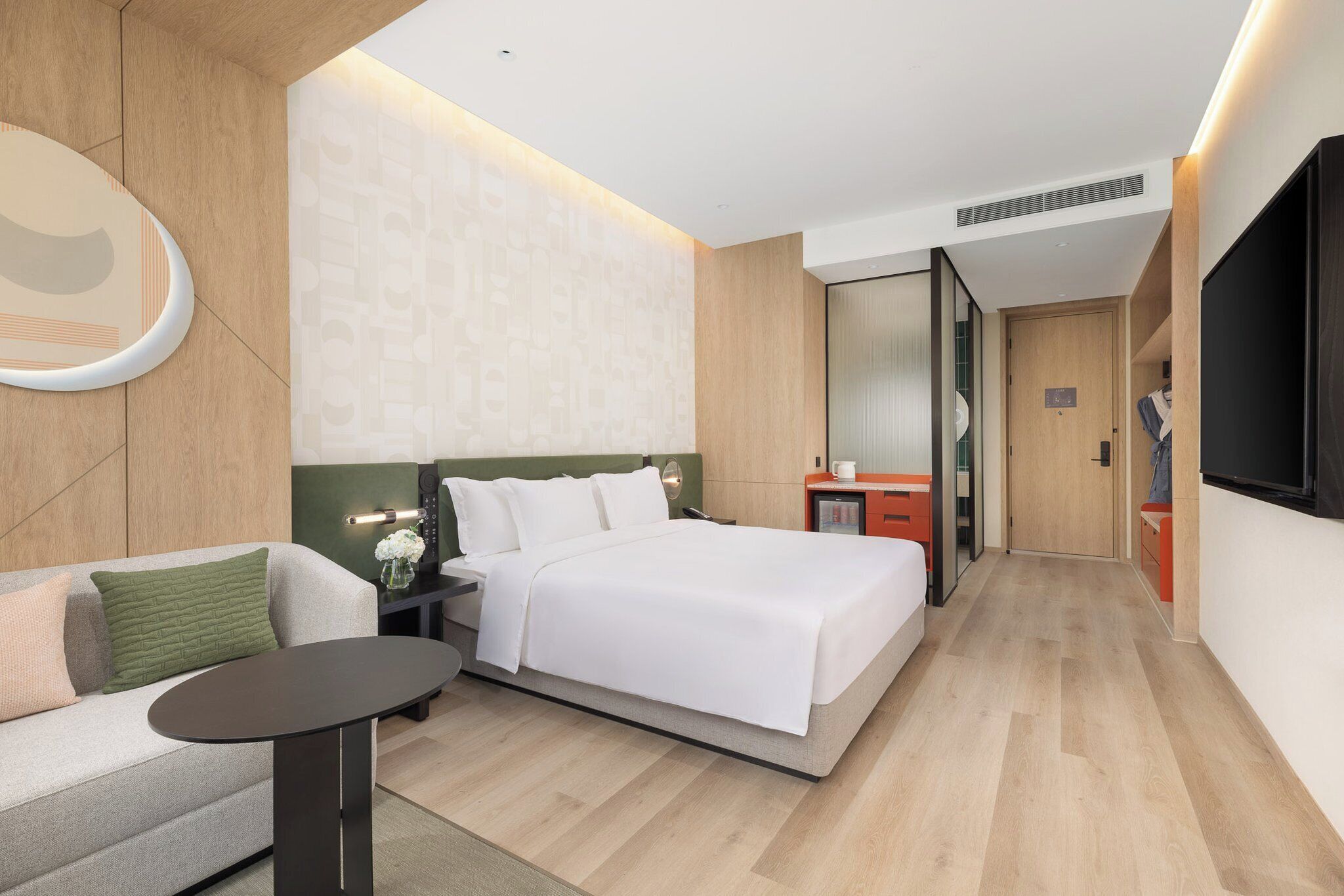 A modern hotel room with a bed, a sofa, a small table, a TV, and a wardrobe.