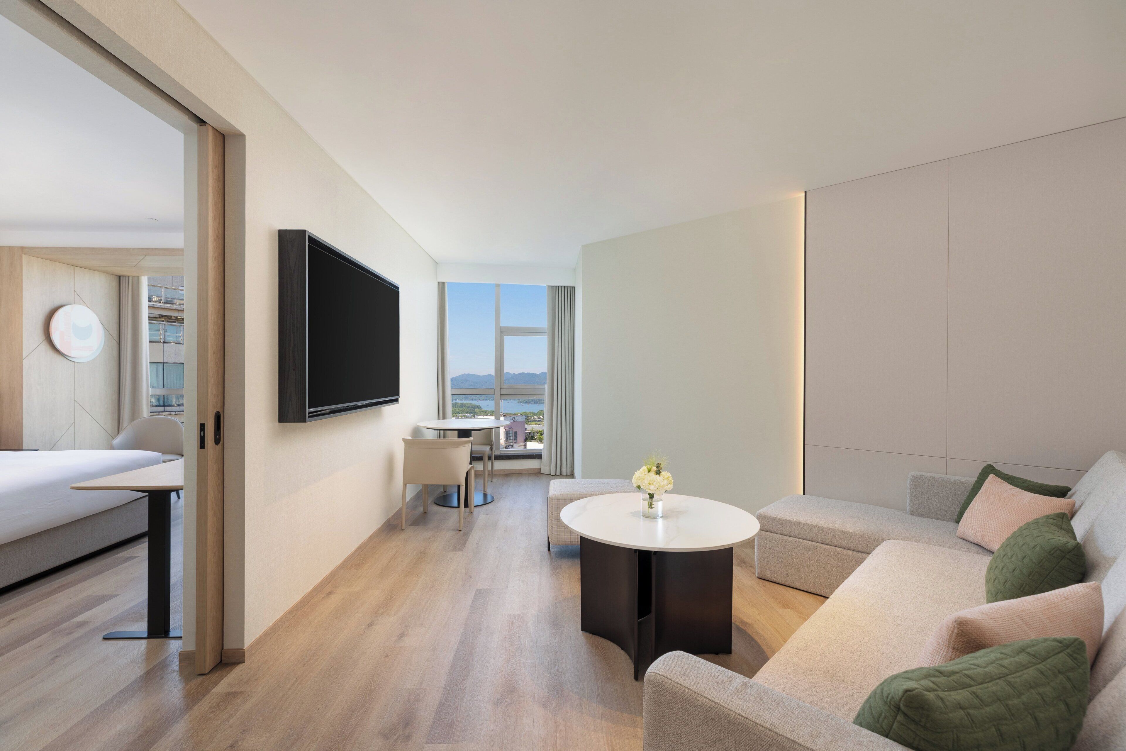 A modern hotel room with a bed, a TV, a dining area, and a sofa.