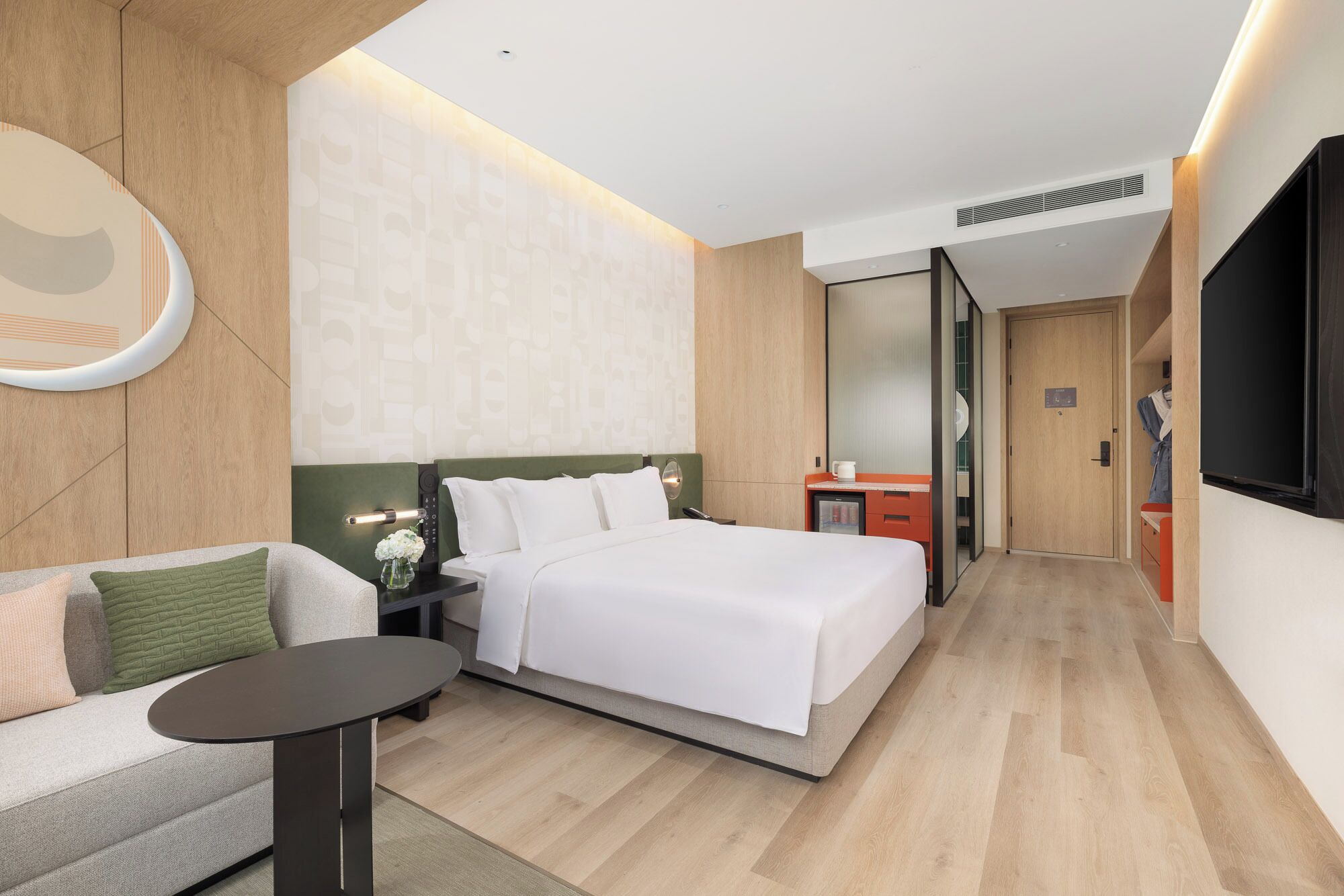 A modern hotel room with a bed, a small table, a sofa, and a TV.