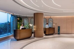 Un moderno área de recepción de hotel con dos mostradores, un pilar grande y vistas al exterior.