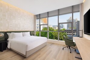Habitación de hotel moderna con una cama grande, un escritorio y vistas de la ciudad a través de amplios ventanales.