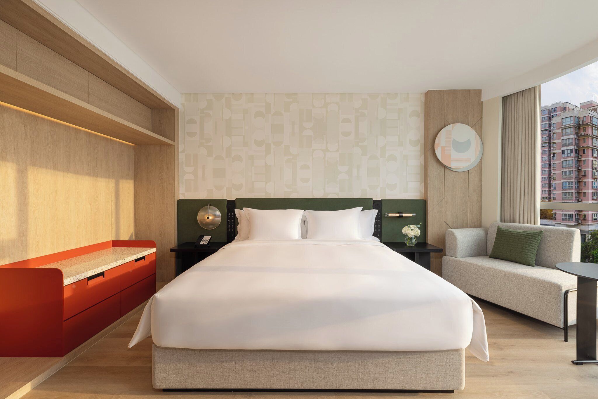 A modern hotel room with a large bed, a sofa, a small table, and a view of the city.