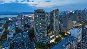 Un edificio alto con varios pisos, rodeado de otros edificios y una masa de agua al fondo.