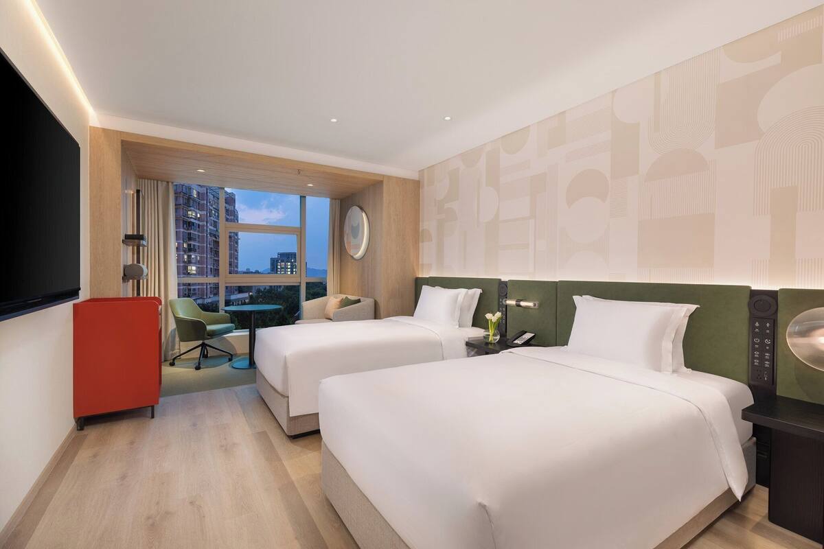 Habitación de hotel con dos camas, un escritorio, una silla, un televisor y vistas a la ciudad.