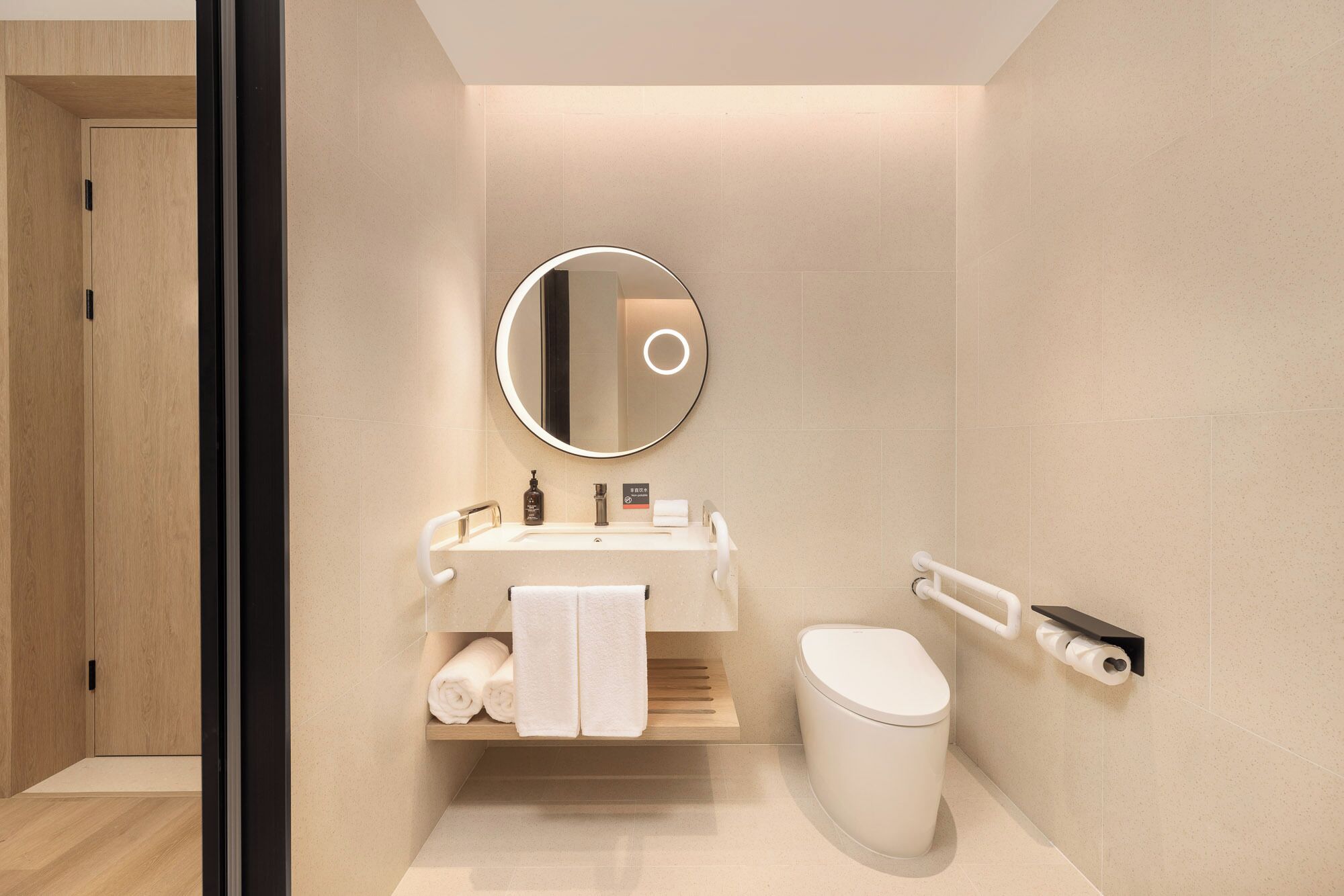 A modern bathroom with a round mirror, white sink, and toilet.