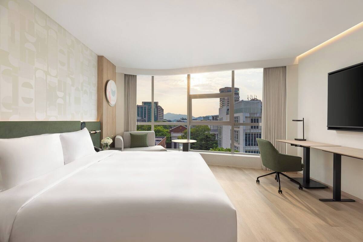 Una habitación de hotel con una cama grande, un escritorio, una silla, una mesita y un televisor.