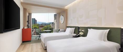 A hotel room with two beds, a TV, a desk, and a view of the city.