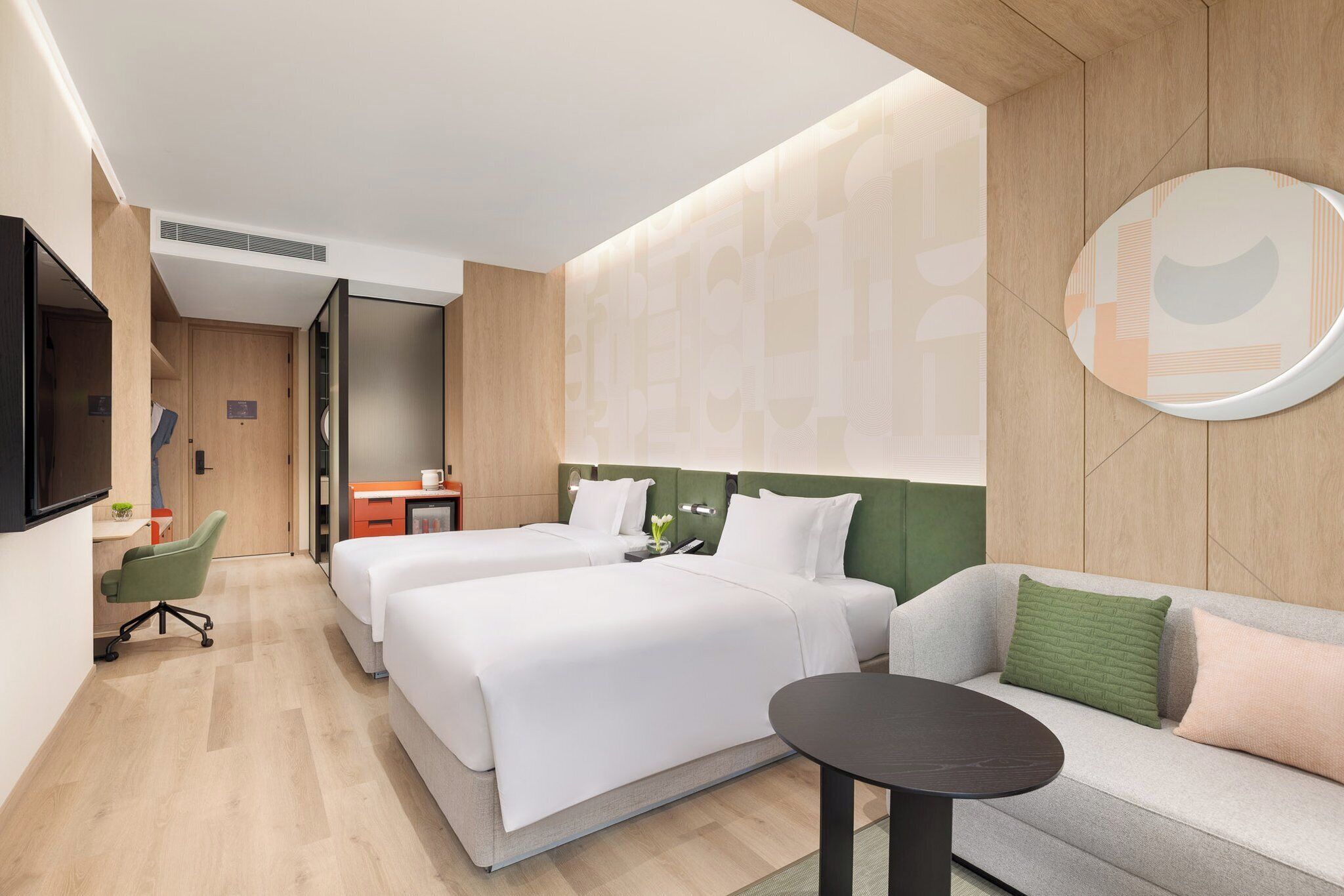 A hotel room with two beds, a sofa, a TV, and a desk with a chair.