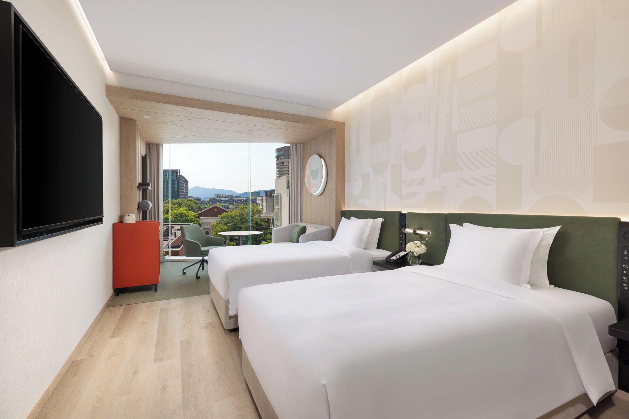 A hotel room with two beds, a desk, a chair, and a view of the city.