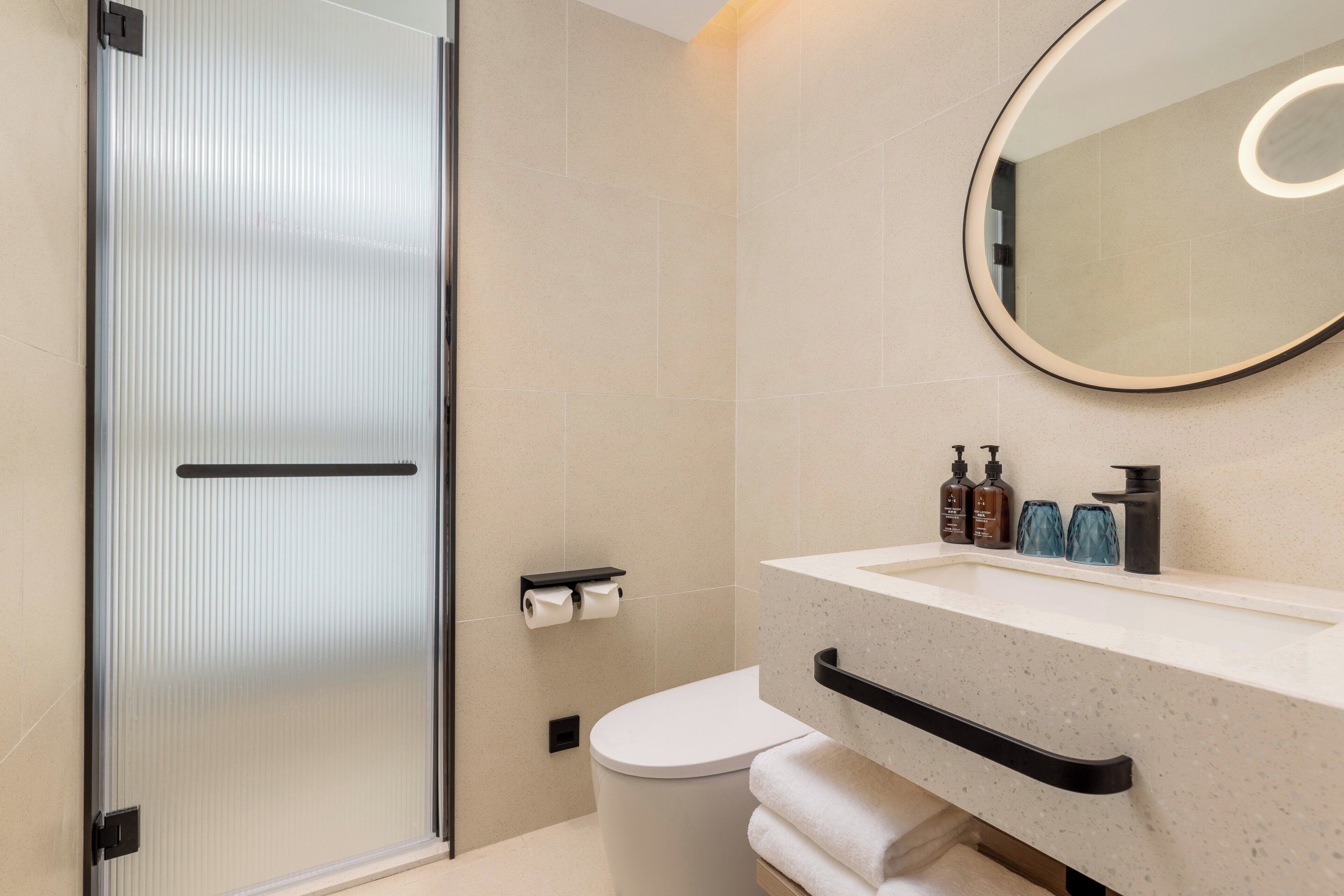 A modern bathroom with a glass shower door, a toilet, a sink with soap dispensers, and a mirror with a light.
