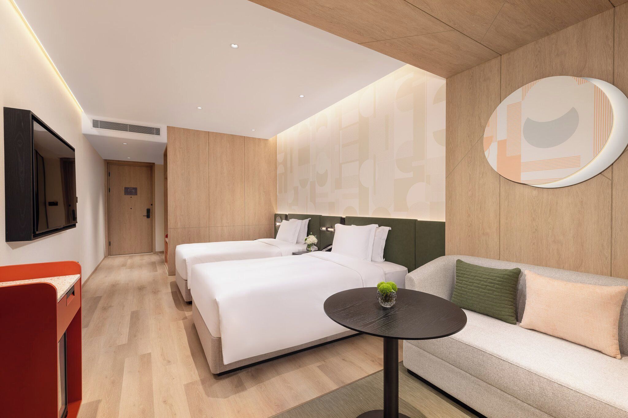 Quarto de hotel moderno com duas camas, um sofá, uma mesinha e uma televisão.