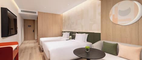 Quarto de hotel moderno com duas camas, um sofá, uma mesinha e uma televisão.