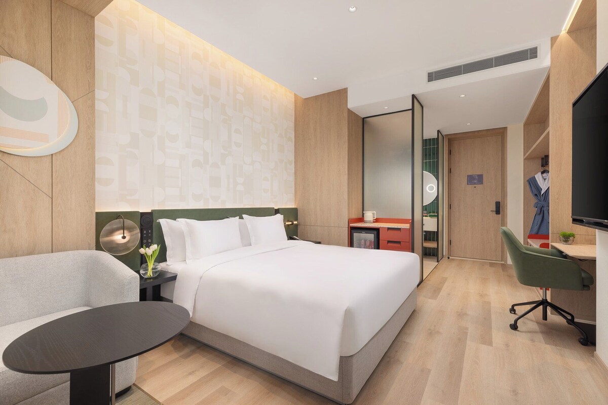 A modern hotel room with a bed, a desk, a chair, and a television.