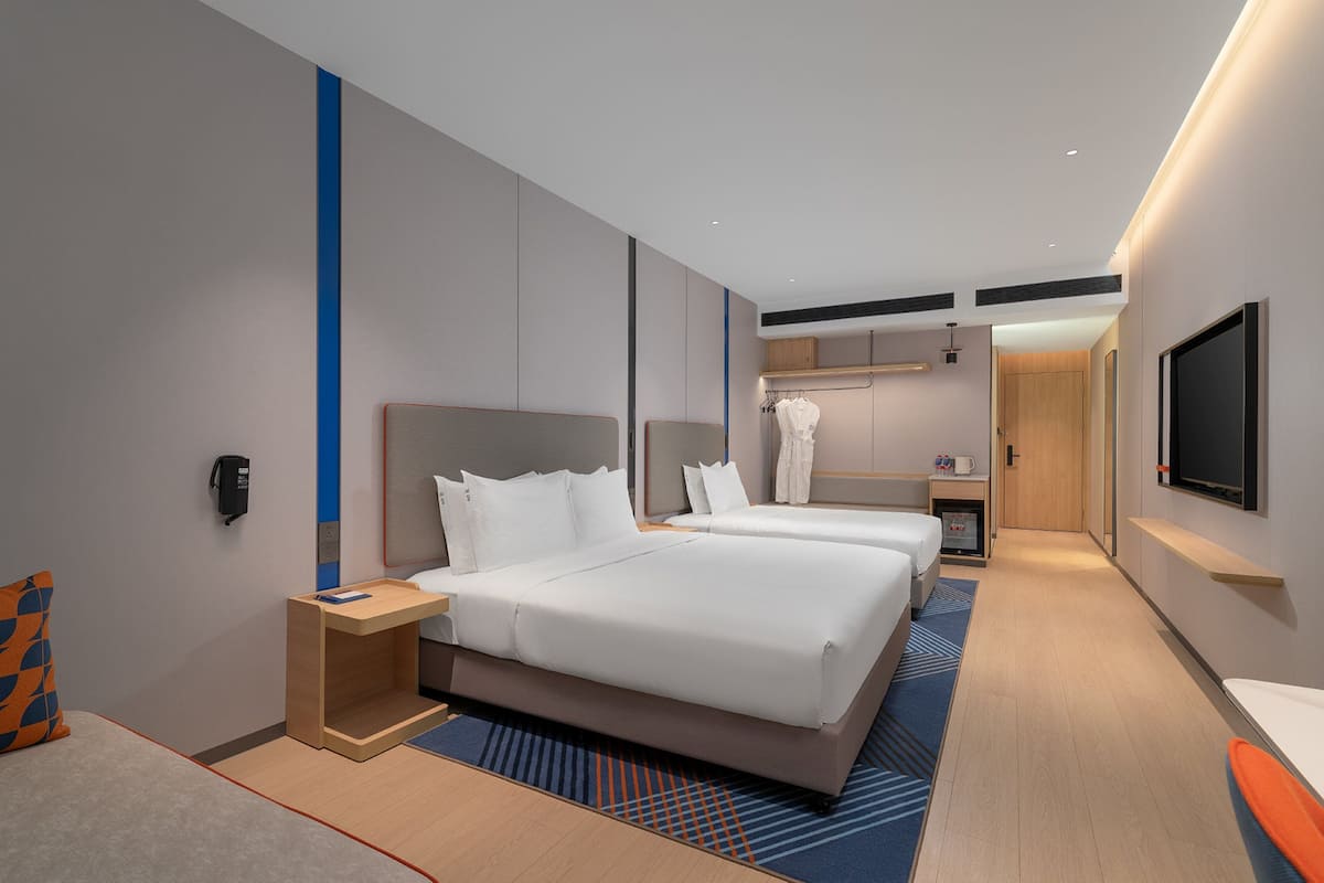 Quarto de hotel moderno com cama grande, escrivaninha, cadeira, televisão e guarda-roupa.