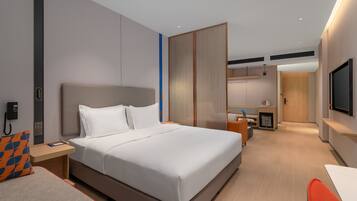 A modern hotel room with a large bed, a desk, a chair, a TV, and a bathroom visible in the background.