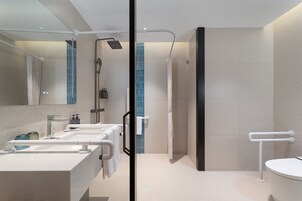 Un baño moderno con un espejo grande, dos lavamanos, una ducha y un inodoro.