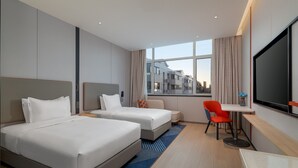 A hotel room with two beds, a desk, a chair, a TV, and a window with a city view.