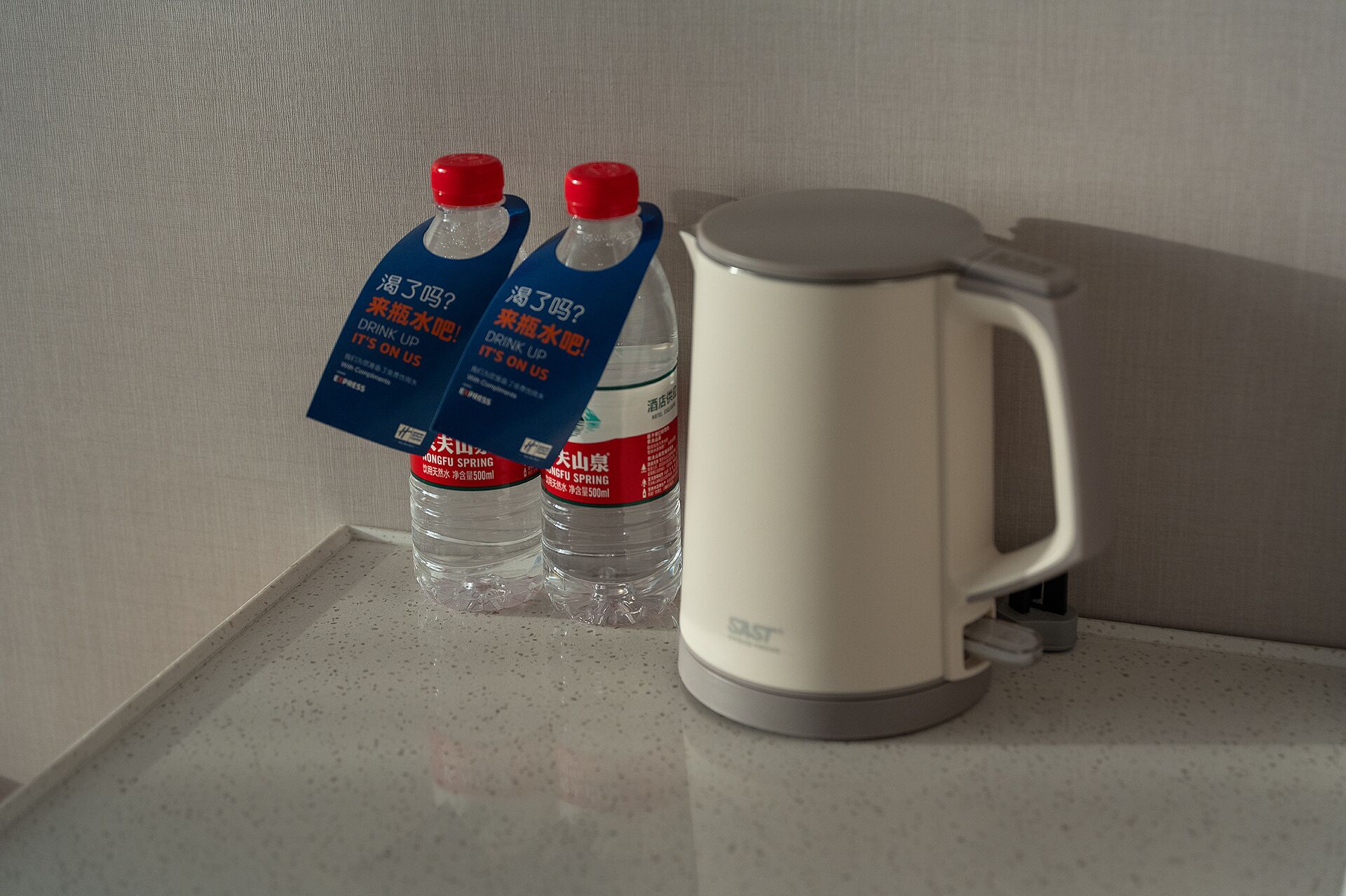 Dos botellas de agua con etiquetas y una tetera eléctrica blanca sobre una encimera.
