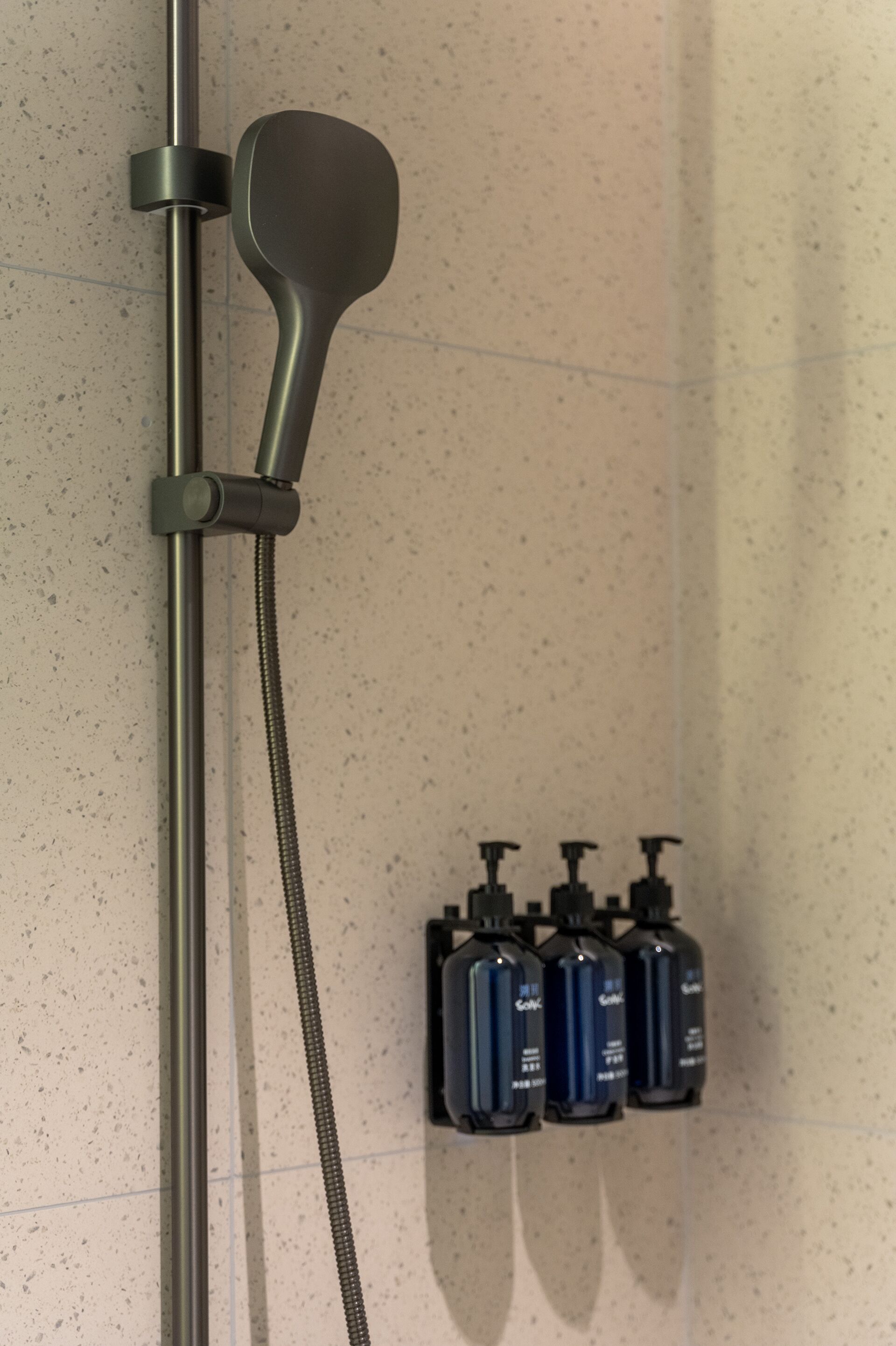 A shower with a handheld showerhead and a wall-mounted soap dispenser.
