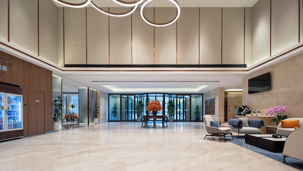 A spacious lobby with a modern design, featuring a reception desk, seating area, and a large window offering a view of the outdoors.