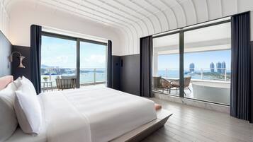 A modern hotel room with a large bed, a balcony with a view of the city, and a table with chairs.