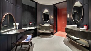 Un baño moderno con paredes oscuras, varios espejos, un lavabo grande y un banco.
