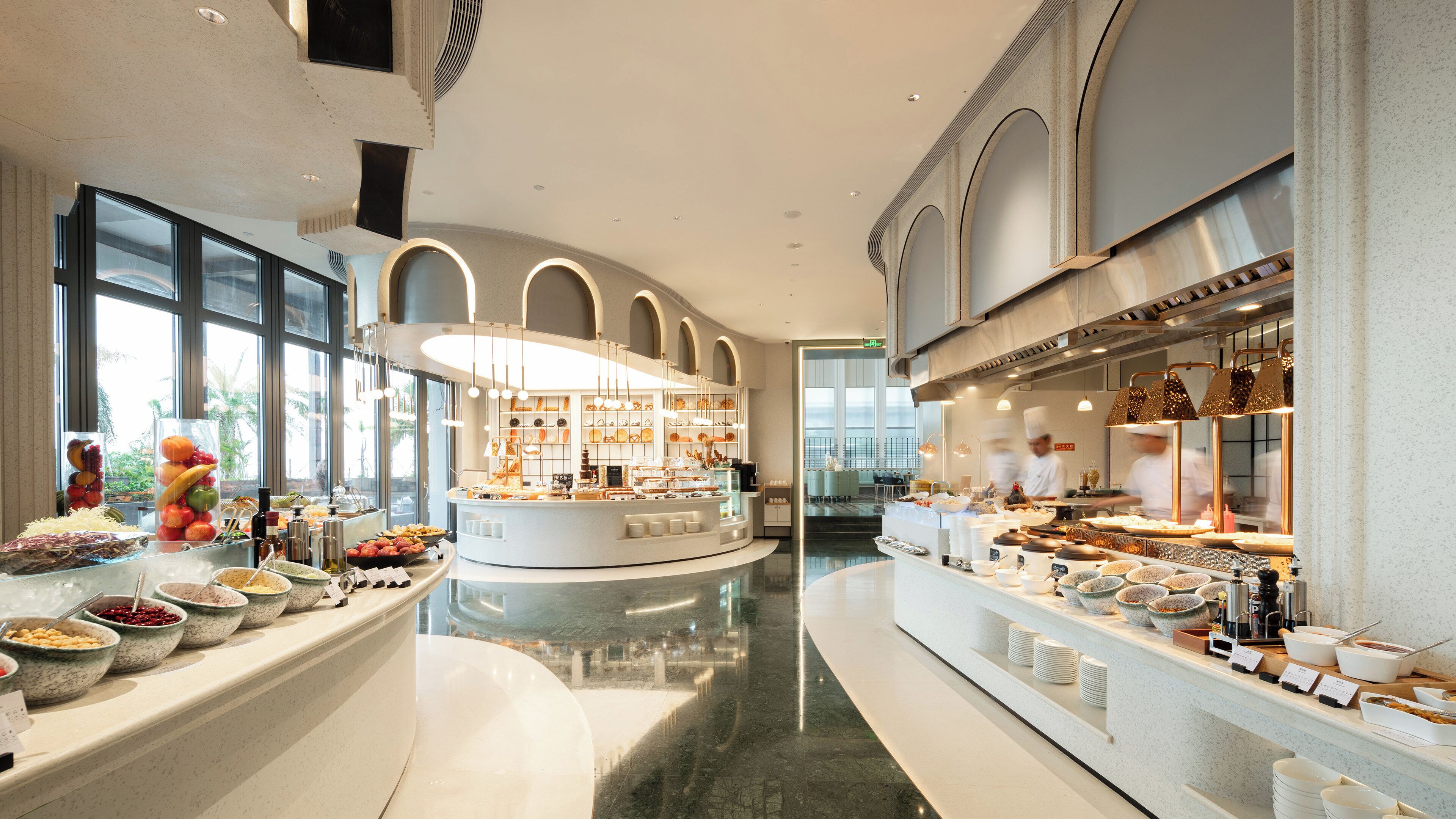 A modern hotel lobby with a central island, large windows, and a kitchen area.