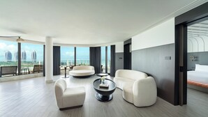 Una habitación de hotel moderna con un balcón grande, un sofá, una mesita de café y una cama con ropa de cama naranja.