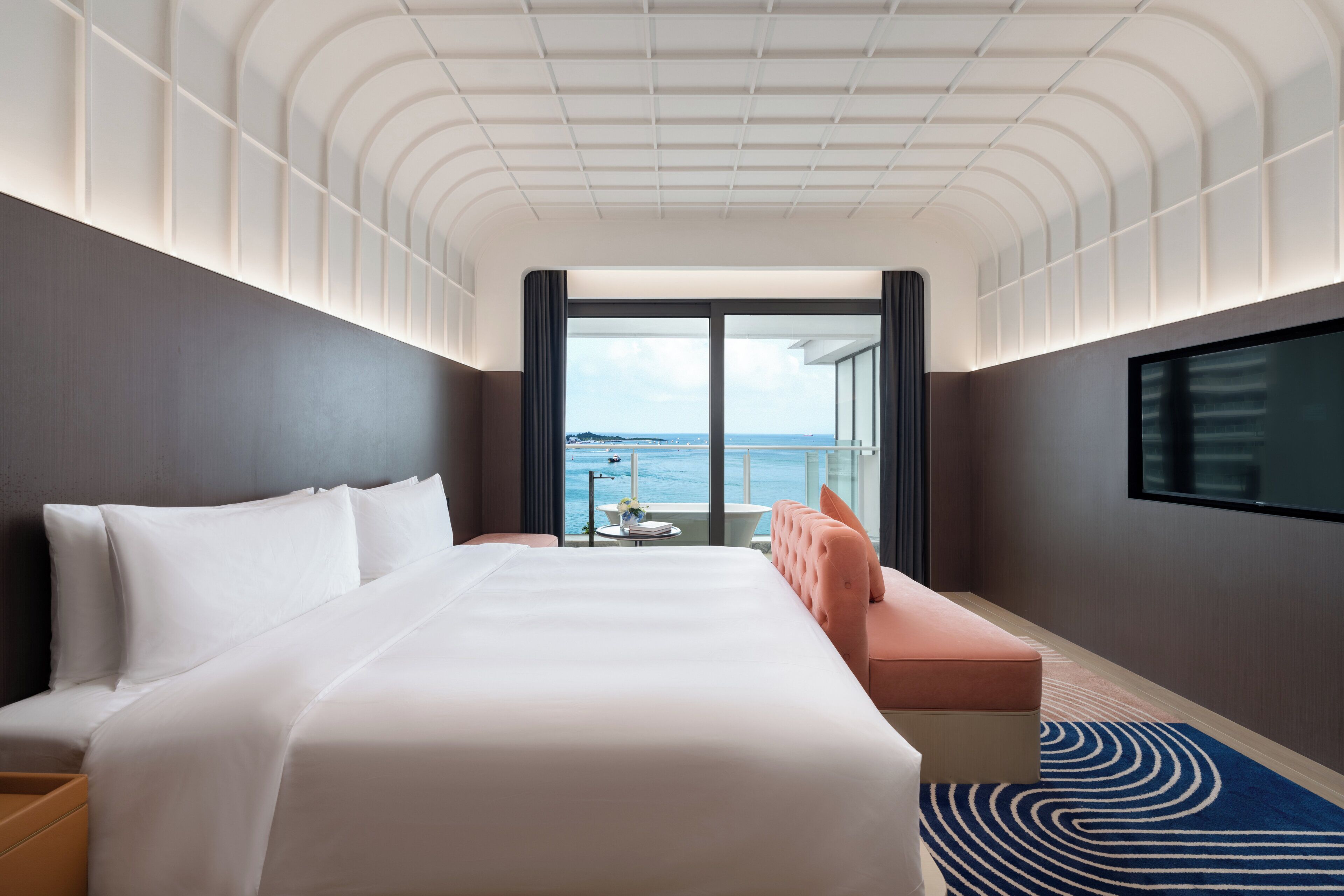 A hotel room with a large bed, a seating area with a view of the sea, and a television on the wall.