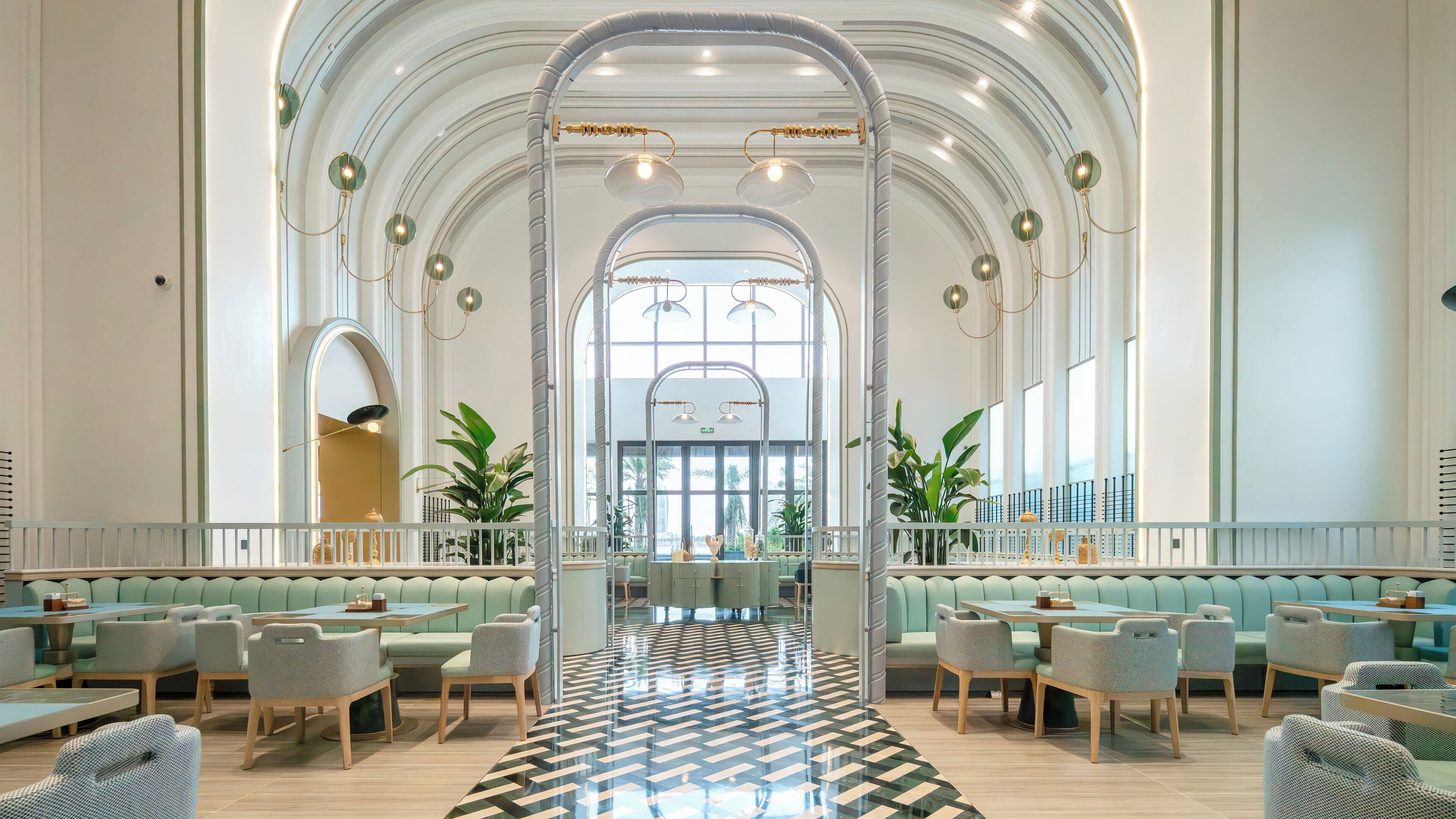 A spacious lobby with high ceilings, arched windows, and a central seating area with tables and chairs.