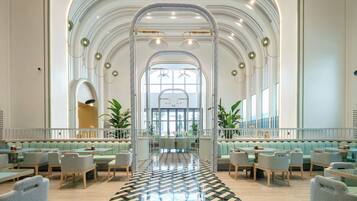 A spacious lobby with high ceilings, arched windows, and a central seating area with tables and chairs.