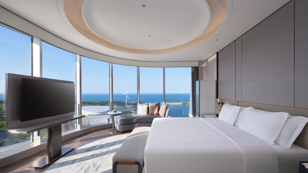 A modern hotel room with a large bed, a flat-screen TV, and a view of the ocean and wind turbines. - Crowne Plaza Weihai Binhai (Weihai)