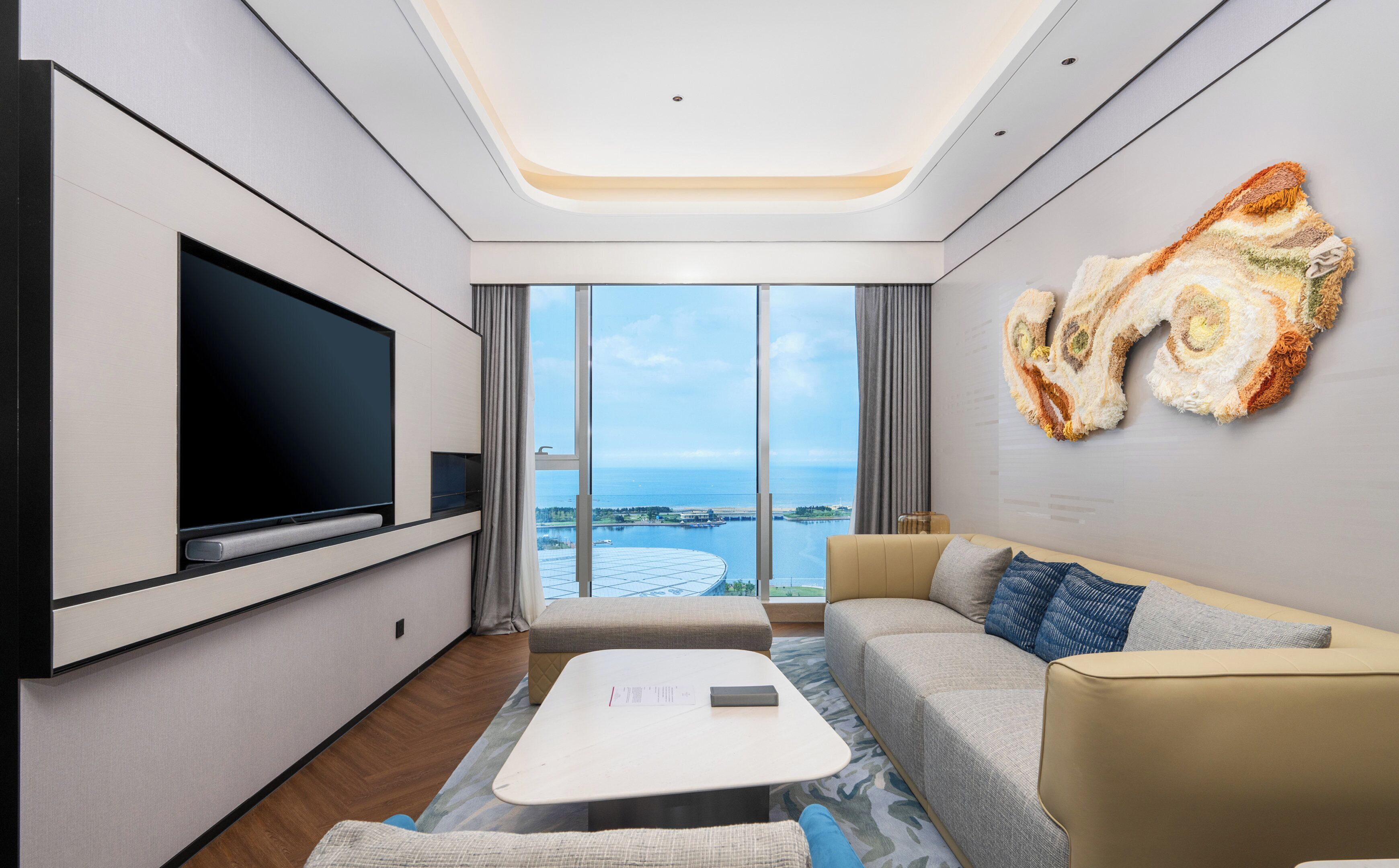 Una sala de estar moderna con un televisor de pantalla plana, un sofá, una mesa de centro y un ventanal con vistas al mar.