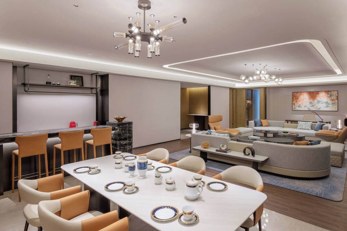 A modern living room with a dining area, featuring a sofa set, a coffee table, and a dining table set for tea.