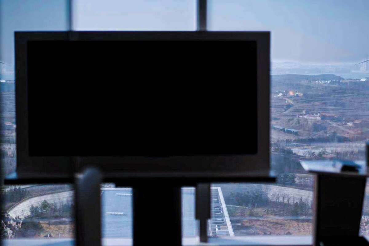 A room with a large window offering a view of a landscape with wind turbines and a bridge.