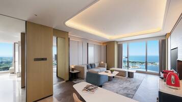 Habitación de hotel moderna con un ventanal que ofrece vista al mar, un sofá, una mesa de centro y un comedor.
