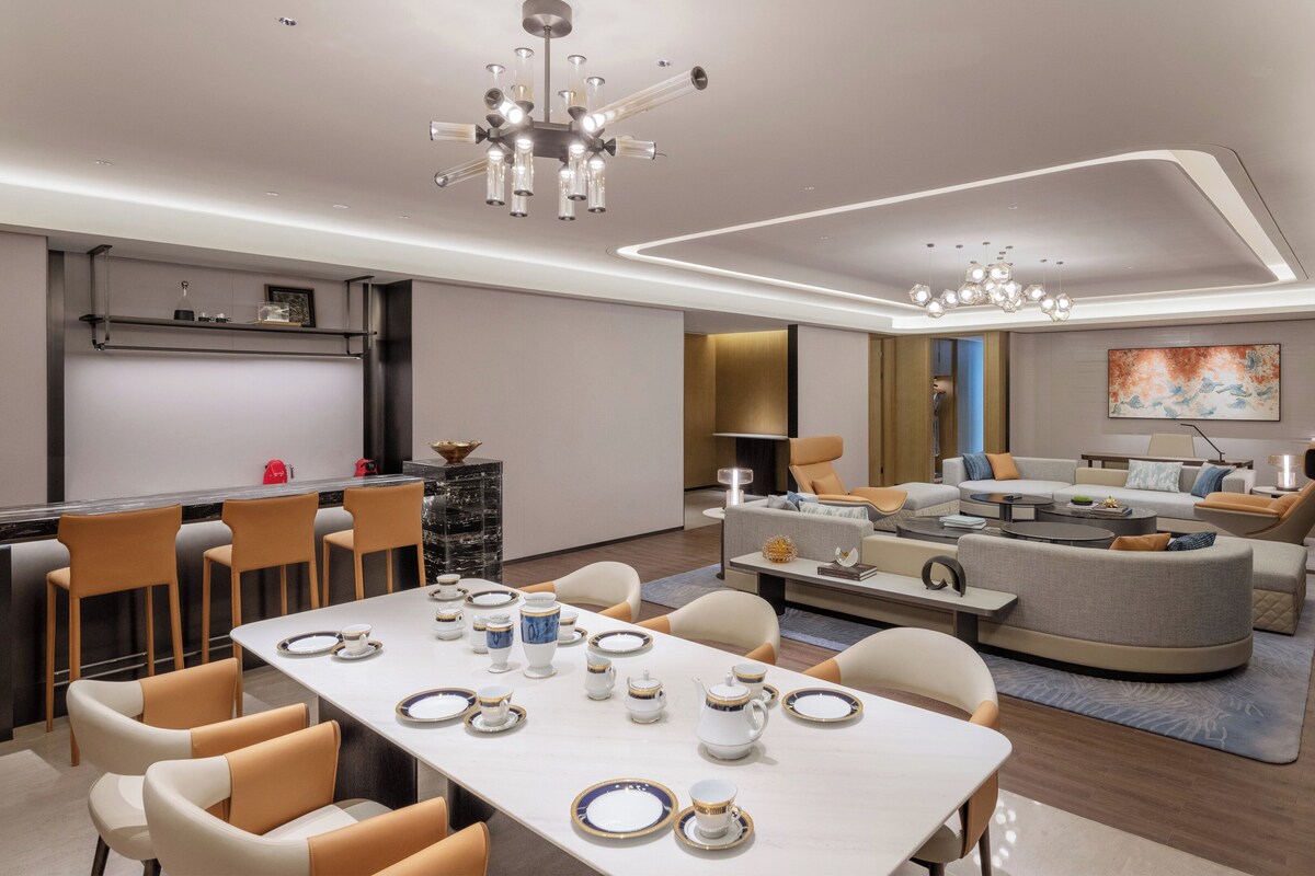 A modern living room with a dining area, featuring a sofa set, a coffee table, and a dining table set for tea.