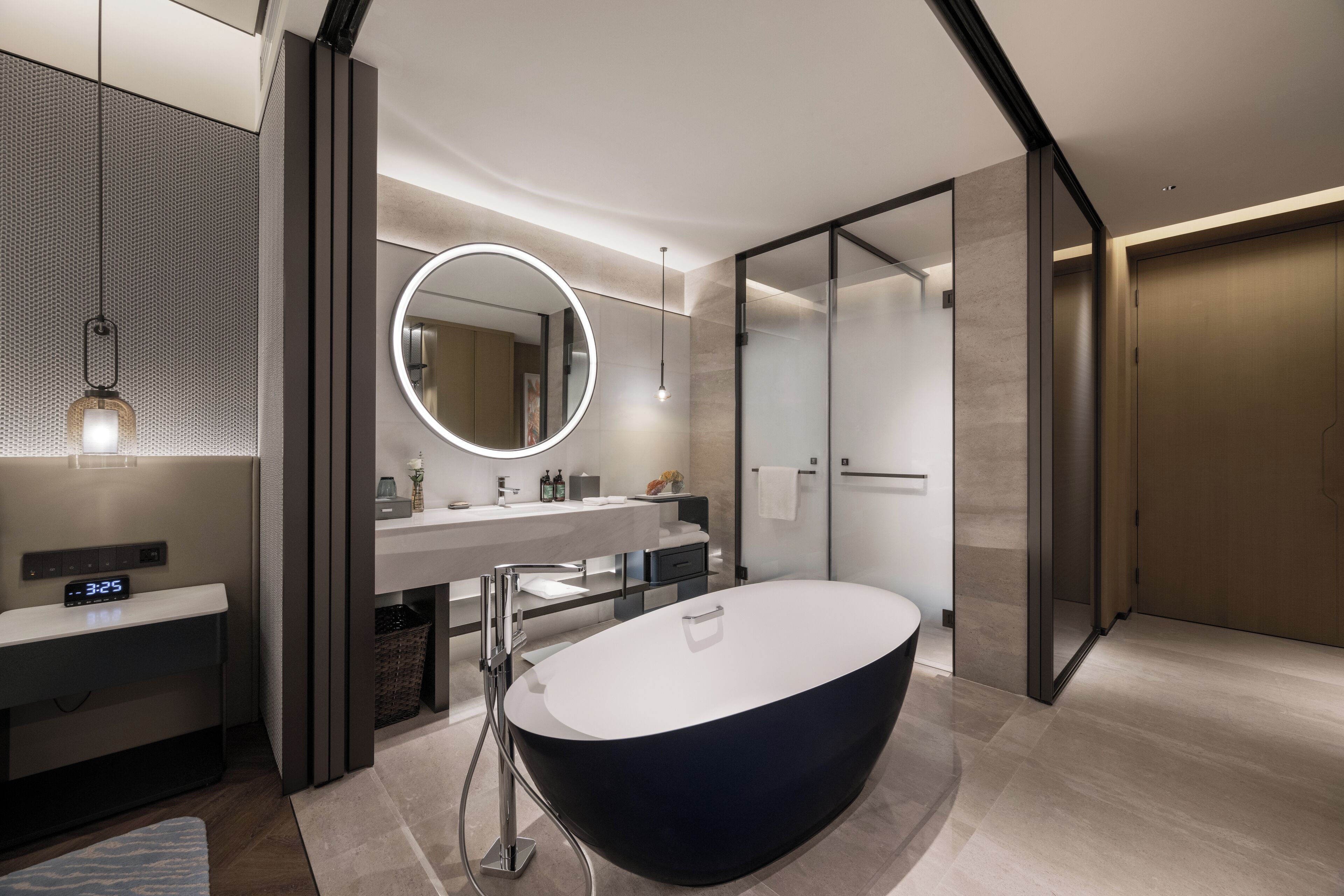 Une salle de bain moderne avec une baignoire sur pieds, un miroir rond et un meuble-lavabo doté d’une horloge numérique.