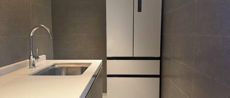Cozinha moderna com pia de aço inoxidável, geladeira embutida e paredes revestidas de azulejos escuros.