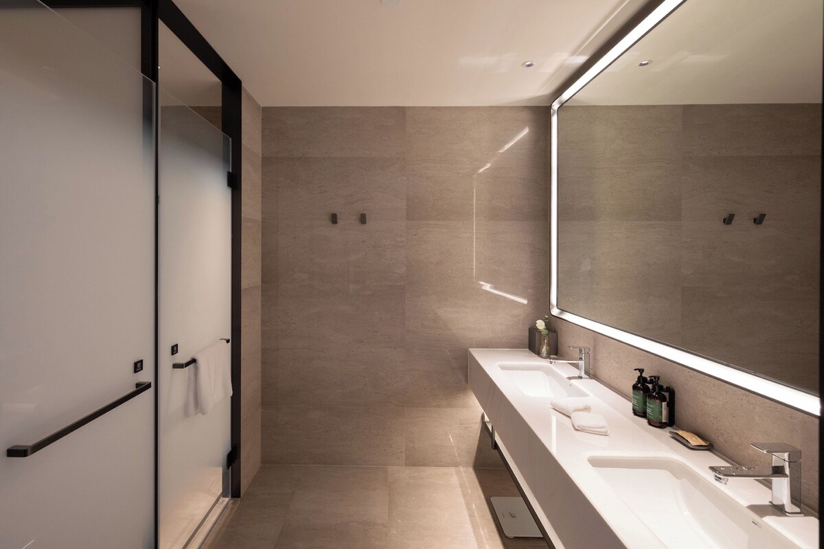 A modern bathroom with a large mirror, two sinks, and a shower area.
