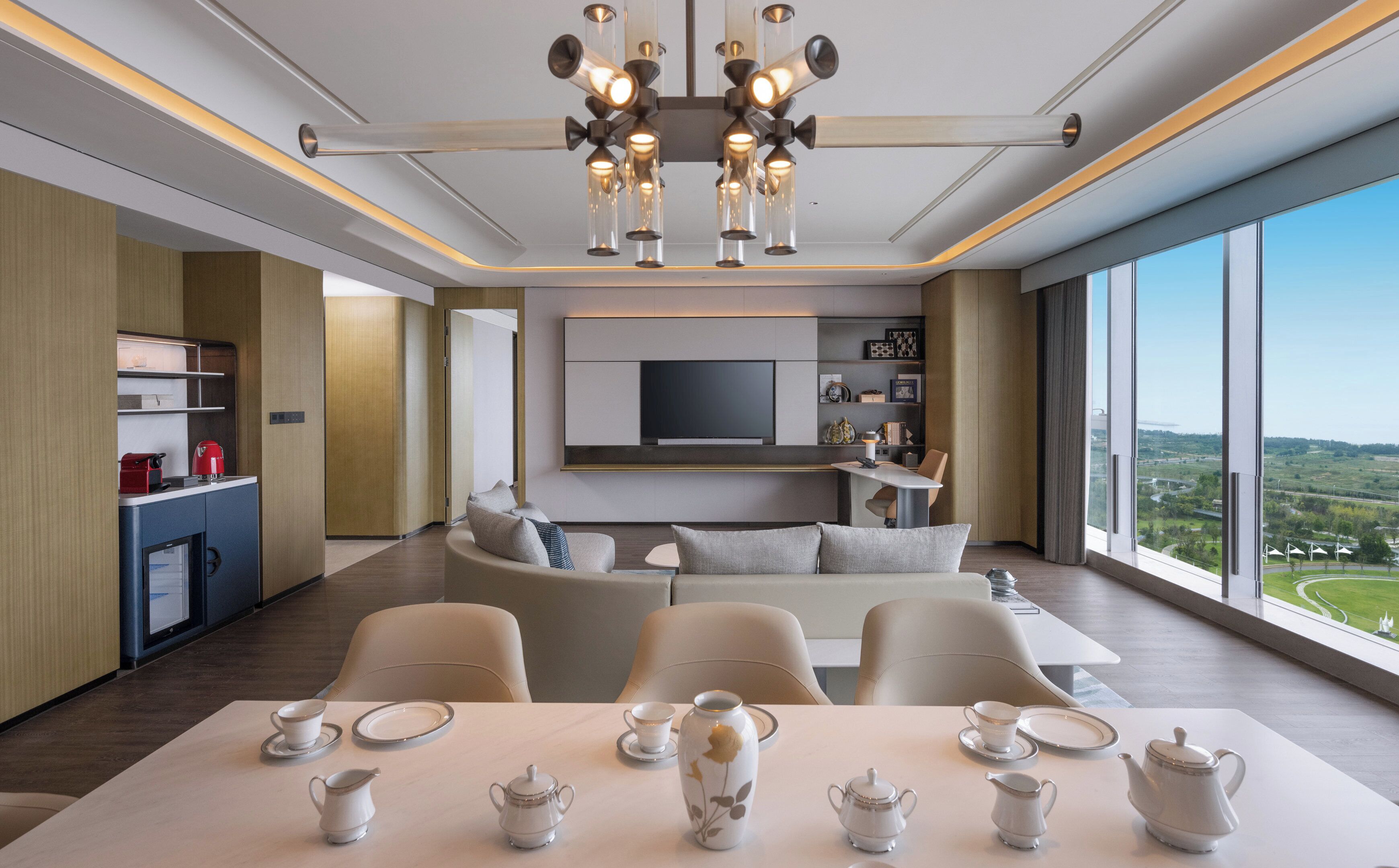 Une chambre d’hôtel moderne dotée d’un coin repas, d’un ensemble de canapés, d’une télévision et offrant une vue sur le paysage.