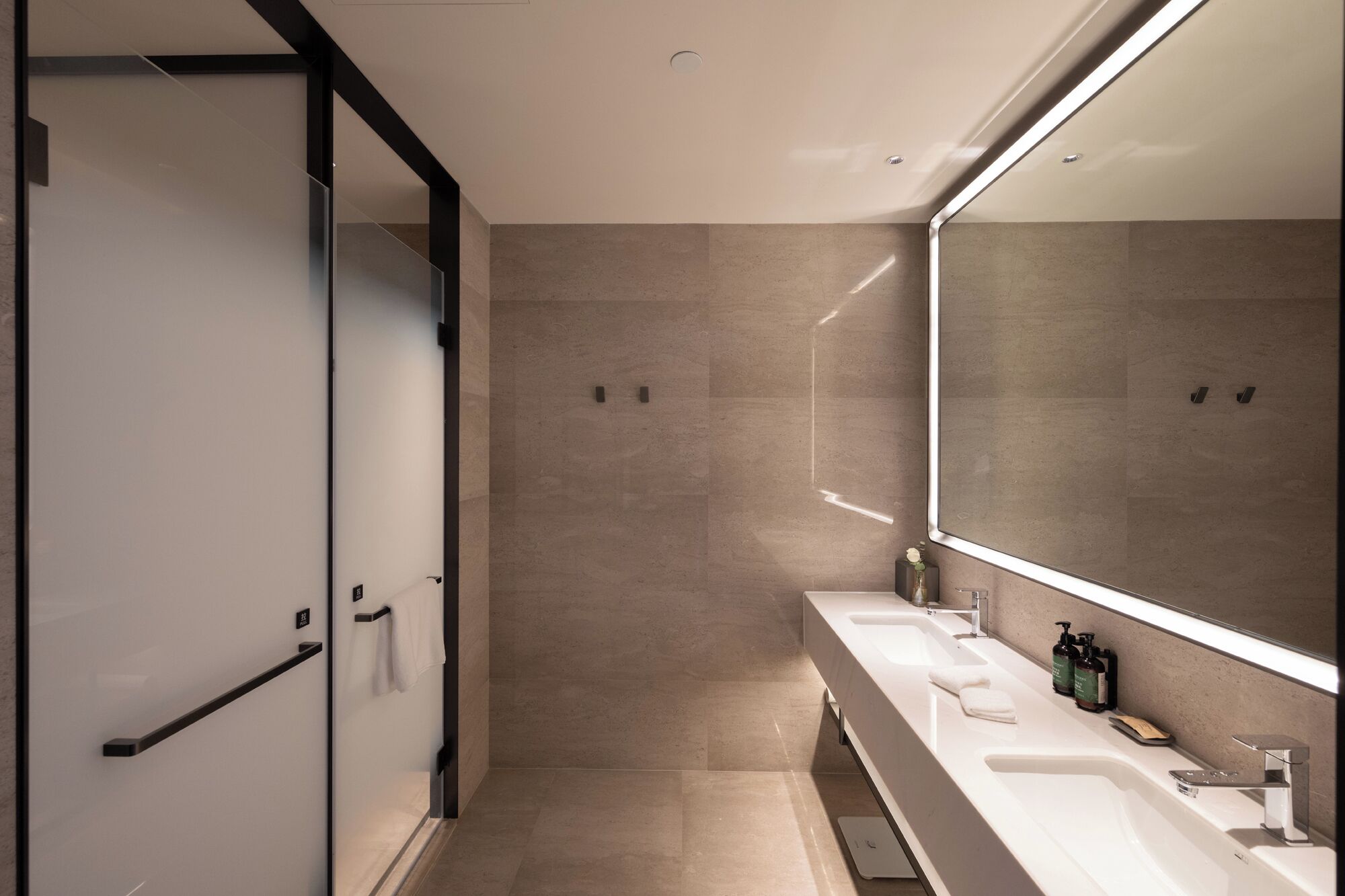 A modern bathroom with a glass shower door, a large mirror, and a vanity with a sink and toiletries.