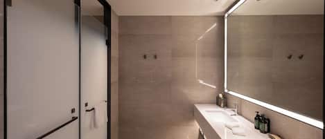 A modern bathroom with a glass shower door, a large mirror, and a vanity with a sink and toiletries.