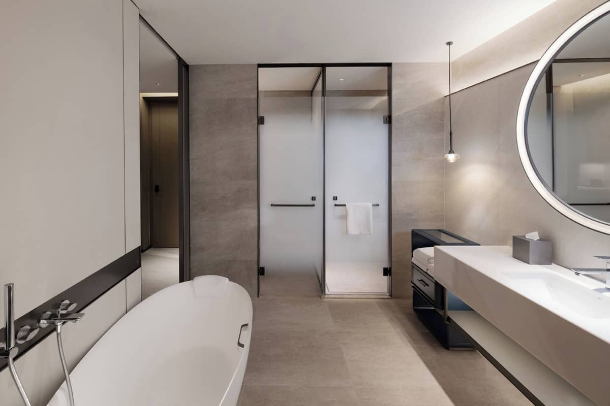 A modern bathroom with a freestanding bathtub, a large mirror, and a vanity with a sink and towel rack.