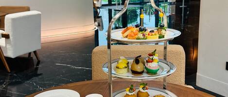 A dining table with a three-tiered dessert stand, plates of fruit, a cup of coffee, and a glass of orange juice.