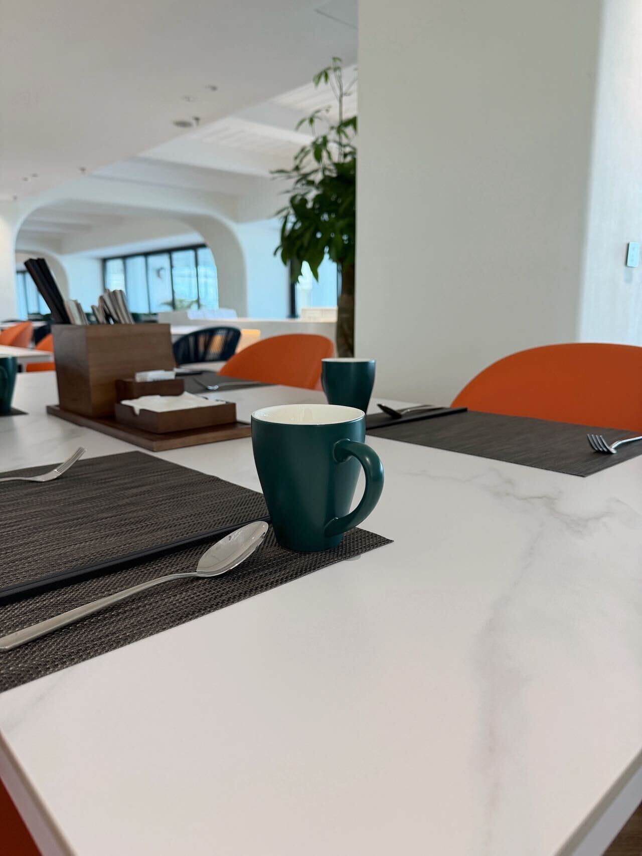 A modern dining area with a white marble table, teal-colored mugs, and orange chairs.