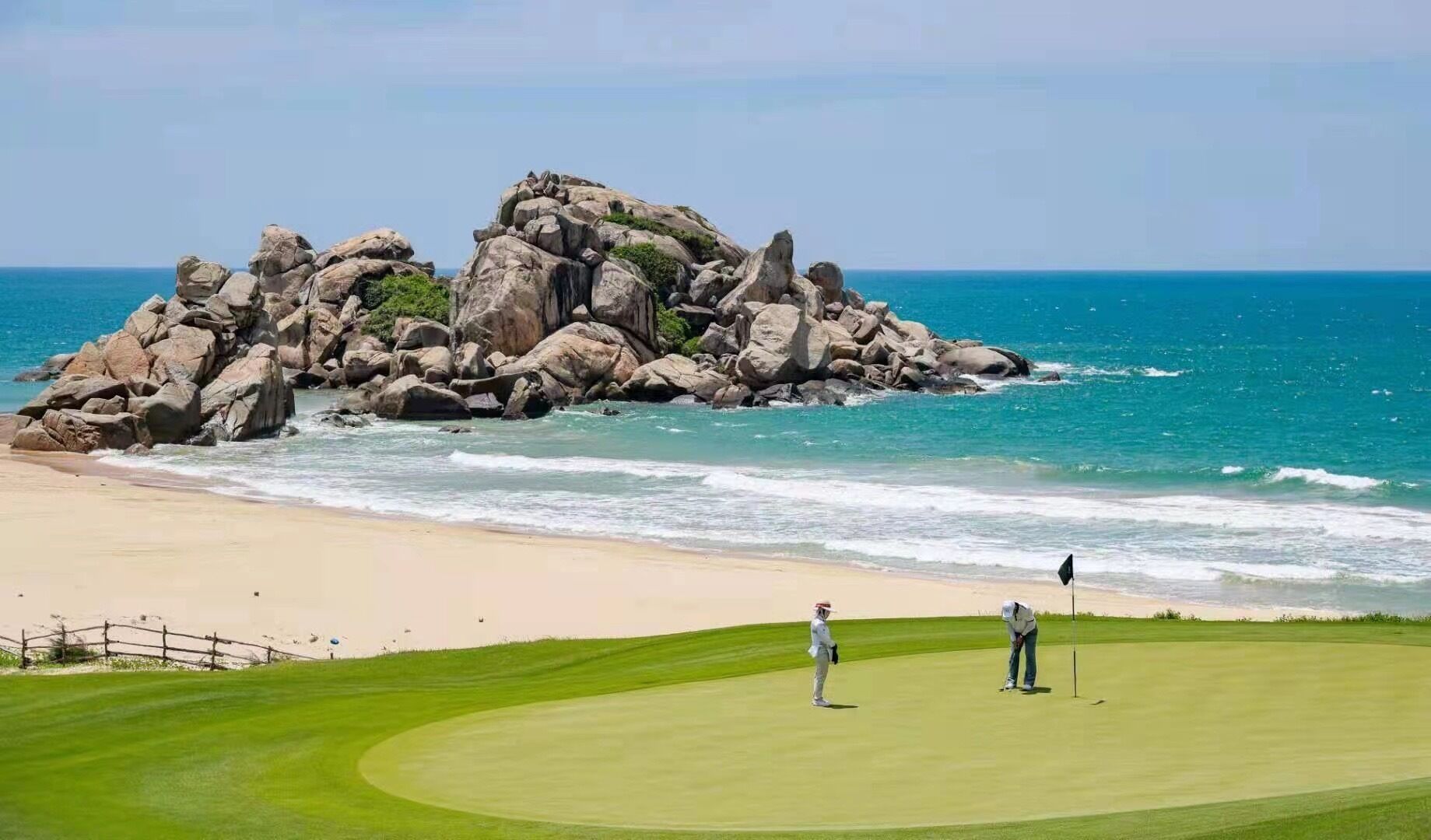 Campo de golf con una gran formación rocosa cerca de la playa y el océano.