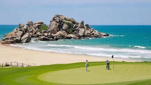 Ein Golfplatz mit einer großen Felsformation in der Nähe von Strand und Ozean.