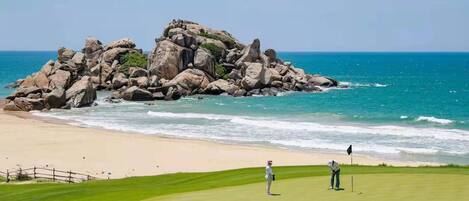 Campo de golf con una gran formación rocosa cerca de la playa y el océano.